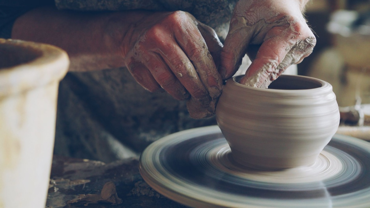 Hands shaping clay on a pottery wheel for a craft-based side job.